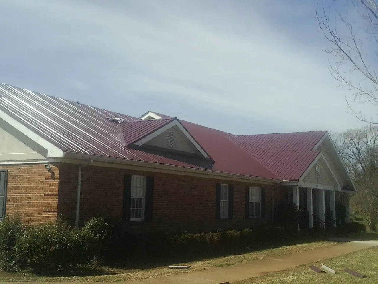 Red metal roof with gabled entries on a long brick building, from a Hail Damage Roof Repair job in Kittitas