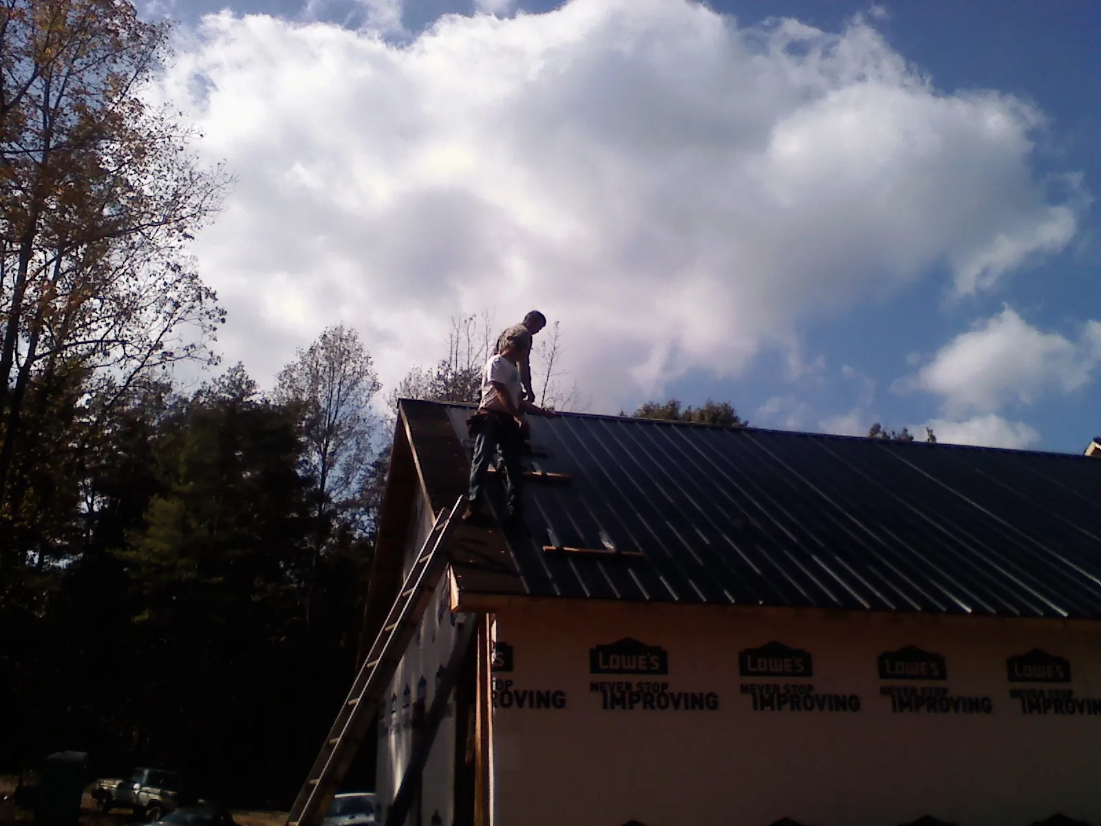 Roofer fastening dark metal panels high against a cloudy sky, from a Roof Inspection job in Kittitas