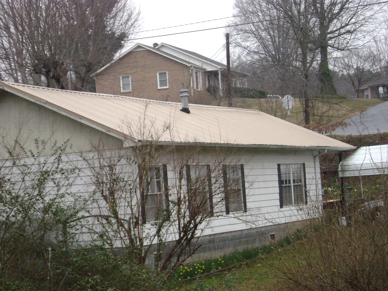 Tan metal roof on a white sided house set into a hillside — Commercial Roofing by Roofing Brothers in Kittitas